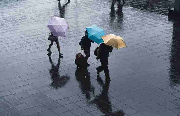 persone si riparano dalla pioggia con gli ombrelli